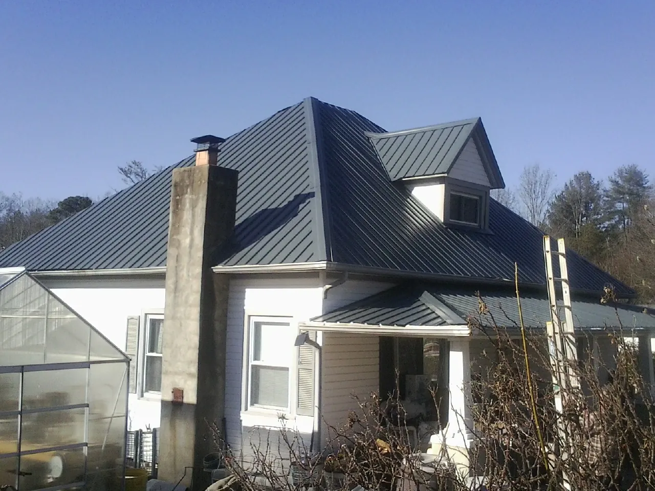 Dark blue standing seam metal roof on a white farmhouse with dormer — Slate & Tile Roof Repair by Roofing Brothers in Bedford